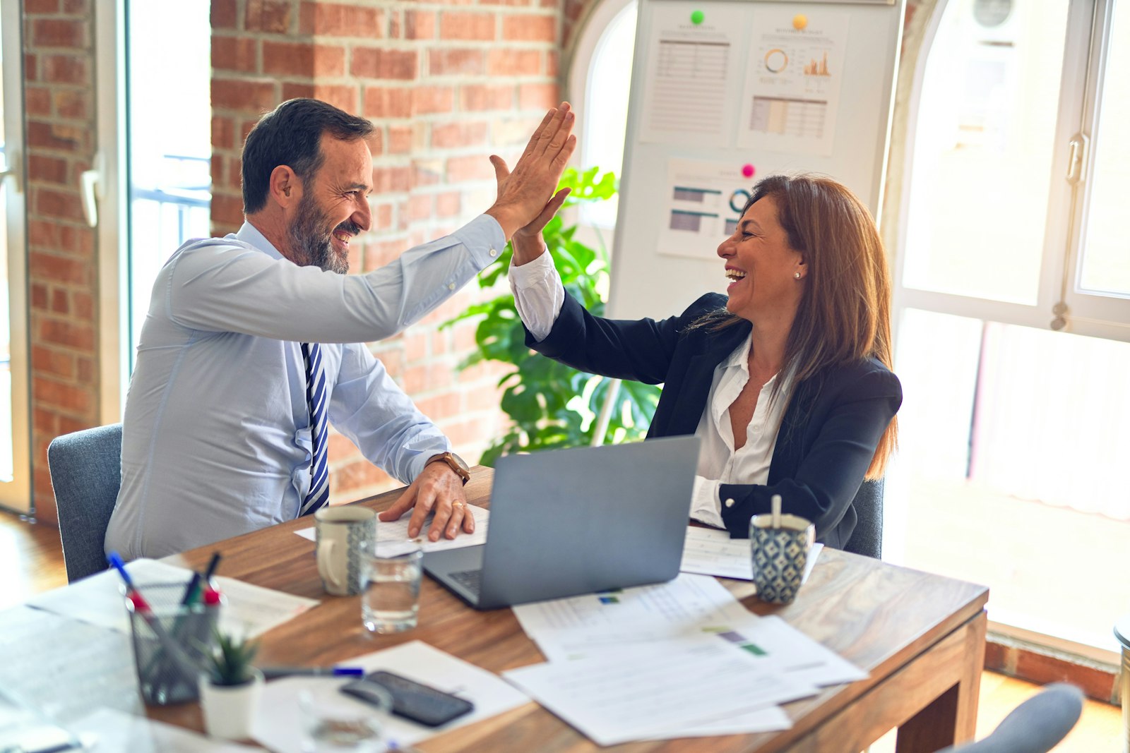 Two colleagues high-fiving at a desk, celebrating a shared win