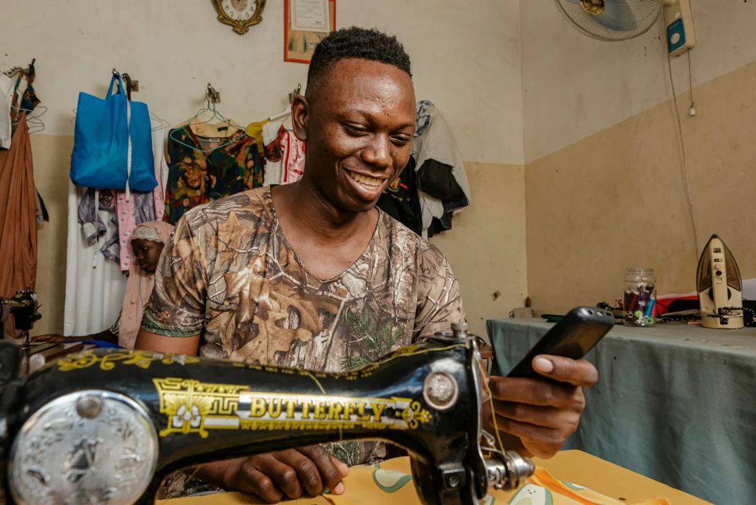 A tailor smiling at his sewing machine in his own shop